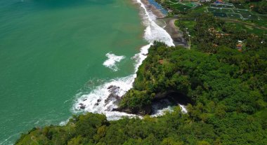 Tepeler ve ağaçlarla kıyı şeridini gösteren hava aracı manzarası, Watu Bale Beach Kebumen Central Java Endonezya 'daki mercan kayalıkları ve deniz dalgaları.
