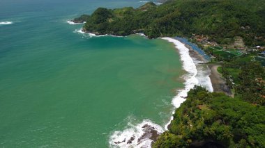 Tepeler ve ağaçlarla kıyı şeridini gösteren hava aracı manzarası, Watu Bale Beach Kebumen Central Java Endonezya 'daki mercan kayalıkları ve deniz dalgaları.