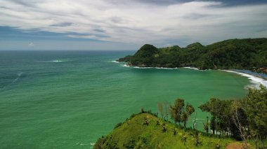 Aerial drone view of coastline with hills and trees, as well as view of coral cliffs and sea with waves from the ocean in Watu Bale Beach Kebumen Central Java Indonesia clipart