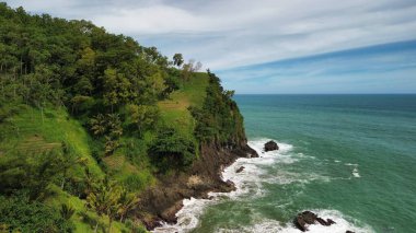 Tepeler ve ağaçlarla kıyı şeridini gösteren hava aracı manzarası, Watu Bale Beach Kebumen Central Java Endonezya 'daki mercan kayalıkları ve deniz dalgaları.