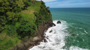 Tepeler ve ağaçlarla kıyı şeridini gösteren hava aracı manzarası, Watu Bale Beach Kebumen Central Java Endonezya 'daki mercan kayalıkları ve deniz dalgaları.