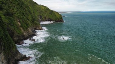 Tepeler ve ağaçlarla kıyı şeridini gösteren hava aracı manzarası, Watu Bale Beach Kebumen Central Java Endonezya 'daki mercan kayalıkları ve deniz dalgaları.