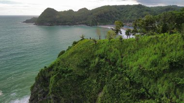 Tepeler ve ağaçlarla kıyı şeridini gösteren hava aracı manzarası, Watu Bale Beach Kebumen Central Java Endonezya 'daki mercan kayalıkları ve deniz dalgaları.