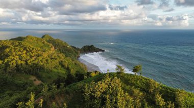 Tepeler ve ağaçlarla kıyı şeridini gösteren hava aracı manzarası, Watu Bale Beach Kebumen Central Java Endonezya 'daki mercan kayalıkları ve deniz dalgaları.