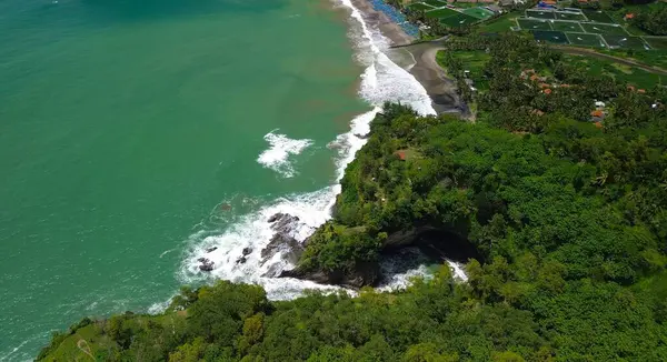 Tepeler ve ağaçlarla kıyı şeridini gösteren hava aracı manzarası, Watu Bale Beach Kebumen Central Java Endonezya 'daki mercan kayalıkları ve deniz dalgaları.