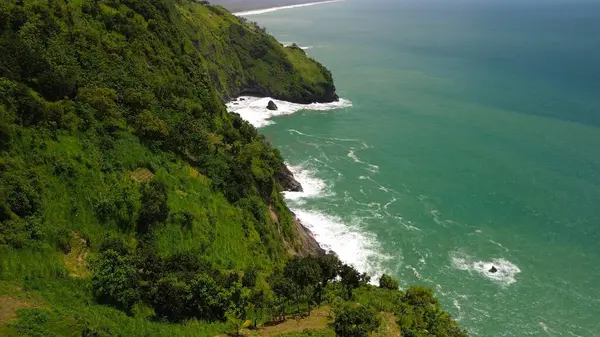 Tepeler ve ağaçlarla kıyı şeridini gösteren hava aracı manzarası, Watu Bale Beach Kebumen Central Java Endonezya 'daki mercan kayalıkları ve deniz dalgaları.