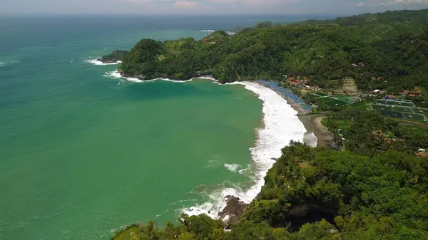 Tepeler ve ağaçlarla kıyı şeridini gösteren hava aracı manzarası, Watu Bale Beach Kebumen Central Java Endonezya 'daki mercan kayalıkları ve deniz dalgaları.