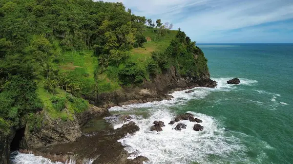 Tepeler ve ağaçlarla kıyı şeridini gösteren hava aracı manzarası, Watu Bale Beach Kebumen Central Java Endonezya 'daki mercan kayalıkları ve deniz dalgaları.