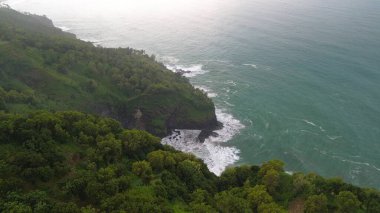 Tepeleri ve ağaçları olan kıyı şeridinin hava aracı görüntüsü, Sagara manzarasında okyanus dalgaları olan mercan kayalıkları ve deniz manzarası, Karang Bolong Beach Kebumen Merkezi Java Endonezya olarak da bilinir.