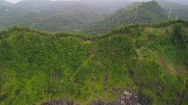 Aerial drone view of coastline with hills and trees, as well as view of coral cliffs and sea with waves from the ocean in Sagara view also known as Karang Bolong Beach Kebumen Central Java Indonesia clipart