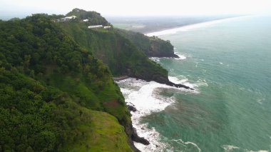 Tepeleri ve ağaçları olan kıyı şeridinin hava aracı görüntüsü, Sagara manzarasında okyanus dalgaları olan mercan kayalıkları ve deniz manzarası, Karang Bolong Beach Kebumen Merkezi Java Endonezya olarak da bilinir.