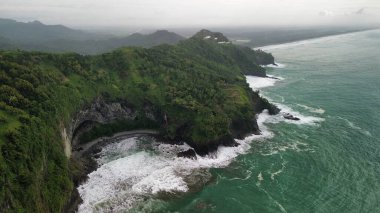 Aerial drone view of coastline with hills and trees, as well as view of coral cliffs and sea with waves from the ocean in Sagara view also known as Karang Bolong Beach Kebumen Central Java Indonesia clipart