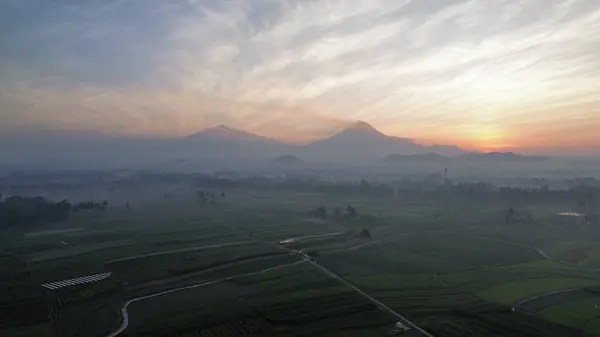 Pirinç tarlalarının ve kırsal alanların insansız hava aracı görüntüsü. Dağların arka planı, güneş doğuşu ve sabah bulutları.