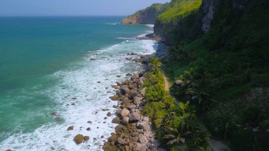  Tepelerin, kayalıkların, ağaçların, kumsalların ve Menganti Sahili, Kebumen, Central Java, Endonezya 'nın deniz ve okyanuslarından gelen dalgaların bulunduğu bir adam.