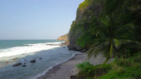 Tepelerin, kayalıkların, ağaçların, kumsalların ve Menganti Sahili, Kebumen, Central Java, Endonezya 'nın deniz ve okyanuslarından gelen dalgaların bulunduğu bir adam.