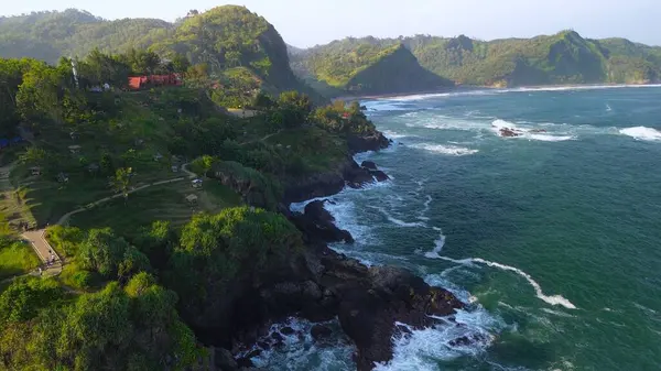  Tepelerin, kayalıkların, ağaçların, kumsalların ve Menganti Sahili, Kebumen, Central Java, Endonezya 'nın deniz ve okyanuslarından gelen dalgaların bulunduğu bir adam.