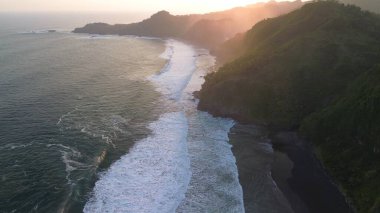  Tepeler, tepeler, kayalıklar, ağaçlar, kumsallar ve Surumanis Sahili, Kebumen, Central Java, Endonezya 'dan deniz ve okyanus dalgalarıyla tepede gün batımı.