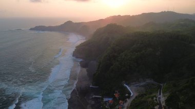  Tepeler, tepeler, kayalıklar, ağaçlar, kumsallar ve Surumanis Sahili, Kebumen, Central Java, Endonezya 'dan deniz ve okyanus dalgalarıyla tepede gün batımı.