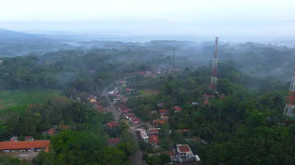Kırsal ve tepelerin dramatik hava aracı görüntüsü sabah sisi ve arka plan olarak dağ aralığı olan yemyeşil ağaçlarla dolu.