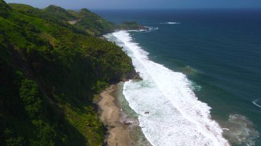 Tepeler ve ağaçlarla dolu kıyı şeridinin hava aracı görüntüsü, mercan kayalıkları ve deniz manzarası, Pecaron Beach Kebumen Central Java Endonezya 'daki okyanus dalgaları.