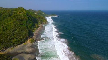 Tepeler ve ağaçlarla dolu kıyı şeridinin hava aracı görüntüsü, mercan kayalıkları ve deniz manzarası, Pecaron Beach Kebumen Central Java Endonezya 'daki okyanus dalgaları.