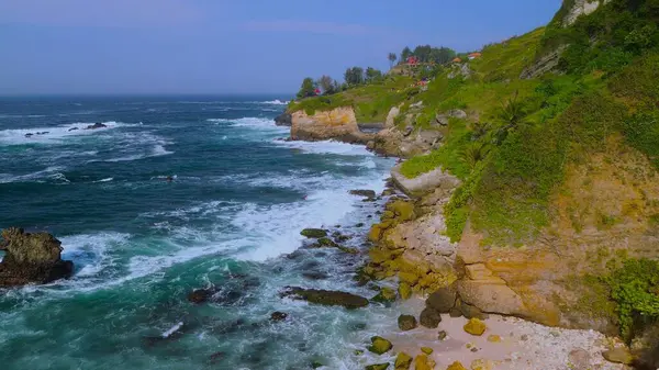 Tepeler ve ağaçlarla dolu kıyı şeridinin hava aracı görüntüsü, mercan kayalıkları ve deniz manzarası, Pecaron Beach Kebumen Central Java Endonezya 'daki okyanus dalgaları.