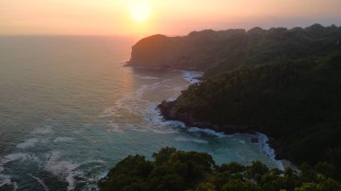 Deniz kenarındaki mercan tepelerinin tepelerinden gün batımının drone görüntüsü ağaçlar, sahil kum mercan kayalıkları ve Sawangan Sahili 'nden gelen dalgalar, Kebumen, Central Java