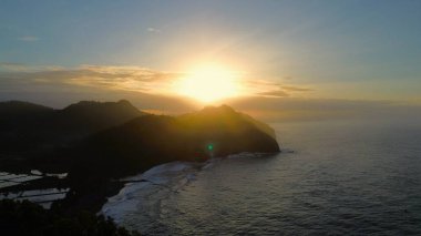 Kıyı şeridinin tepelerinde kuş bakışı güneş doğuyor tepeler, ağaçlar, uçurumlar, mercan resifleri ve deniz dalgaları Surumanis Sahili, Kebumen, Central Java