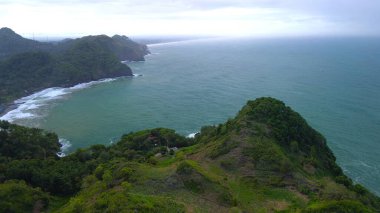 Tepeler, ağaçlar, kayalıklar, mercan resifleri ve Surumanis Sahili, Kebumen, Central Java 'daki denizden gelen dalgalarla birlikte kuş bakışı kıyı şeridi manzarası