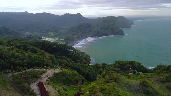 Tepeler, ağaçlar, kayalıklar, mercan resifleri ve Surumanis Sahili, Kebumen, Central Java 'daki denizden gelen dalgalarla birlikte kuş bakışı kıyı şeridi manzarası