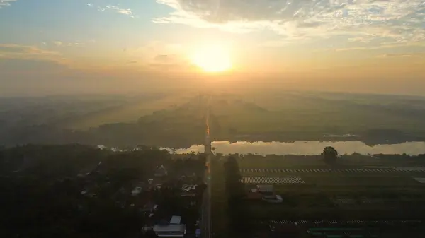 Arka planda güneş doğarken ve sabah sisi varken Medono Nehri 'ni geçen karayolu ve köprünün hava aracı görüntüsü