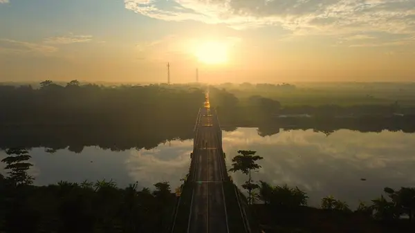 Arka planda güneş doğarken ve sabah sisi varken Medono Nehri 'ni geçen karayolu ve köprünün hava aracı görüntüsü