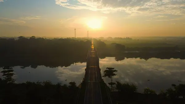 Arka planda güneş doğarken ve sabah sisi varken Medono Nehri 'ni geçen karayolu ve köprünün hava aracı görüntüsü