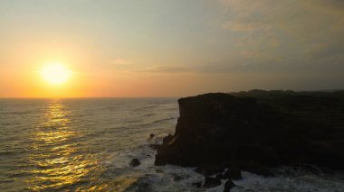 Krakal Beach, Gunung Kidul, Yogyakarta 'daki deniz dalgalarıyla okyanusun kenarında gün batımına bakan kuş bakışı.