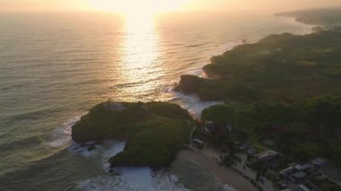 Krakal Sahili, Gunung Kidul, Yogyakarta 'daki deniz dalgalarıyla okyanusun kenarında gün batımını gösteren hava aracı.