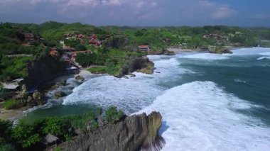 Mbuluk Sahili 'nin insansız hava aracı görüntüsü Gunung Kidul Yogyakarta tepeleri, beyaz kumları, mercan kayalıkları ve ünlü bir turizm merkezi olan okyanus dalgalarıyla dolu bir plaj.
