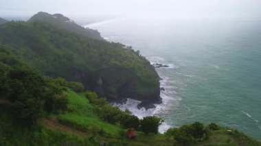 İnsansız hava aracı manzaralı seyahat rotası, tepeli ve ağaçlı kıyı şeridi, okyanustan gelen dalgalar mercan resiflerine çarpıyor, Jerit Hill ve Beach Kebumen Central Java Endonezya