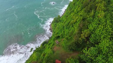 İnsansız hava aracı manzaralı seyahat rotası, tepeli ve ağaçlı kıyı şeridi, okyanustan gelen dalgalar mercan resiflerine çarpıyor, Jerit Hill ve Beach Kebumen Central Java Endonezya