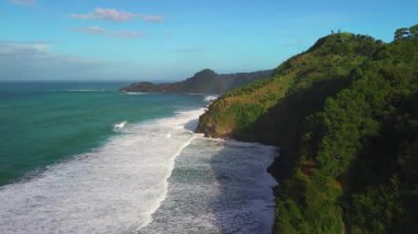 Surumanis Sahili, Kebumen, Central Java, Endonezya 'nın insansız hava aracı manzarası, ağaçlar, mercan resifleri ve okyanustan gelen dalgalarla çevrili bir turizm merkezi.