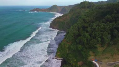 Surumanis Sahili, Kebumen, Central Java, Endonezya 'nın insansız hava aracı manzarası, ağaçlar, mercan resifleri ve okyanustan gelen dalgalarla çevrili bir turizm merkezi.