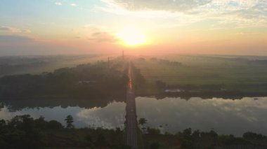 Hava aracı görüntüsü dramatik gün doğumu ve sabah altın saati, tarımsal arazisi olan kırsal bir alanda, ortada bir otoyol ve nehri geçen bir köprü ile.