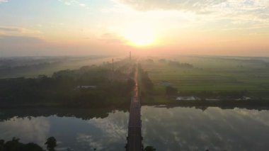 Hava aracı görüntüsü dramatik gün doğumu ve sabah altın saati, tarımsal arazisi olan kırsal bir alanda, ortada bir otoyol ve nehri geçen bir köprü ile.