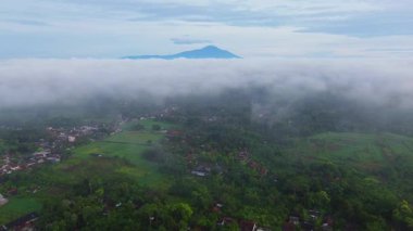 POV hava aracı sisli köyün üzerinde uçuyor ve sabahları arka planda dağlarla birlikte konut kompleksi kuruyor.