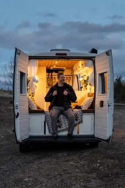 Mature man sitting in the back of a camper van during sunset. Concept van life, lifestyle, people, transportation, vacations, tourism