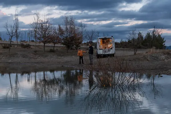 Father and son play throwing stones into the lake at sunset during their camper van vacation. Concept van life, lifestyle, people, transportation, vacations, tourism