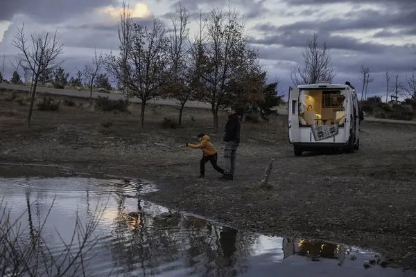 Father and son play throwing stones into the lake at sunset during their camper van vacation. Concept van life, lifestyle, people, transportation, vacations, tourism