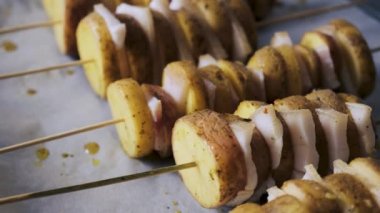Demonstration of sliced potatoes and lard in thin slices on wooden skewers for baking. Close-up