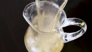 A man pours stewed fruit into a glass carafe. Close-up
