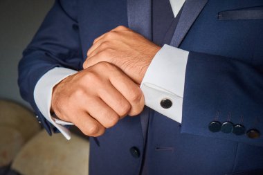 The hand of the groom in a suit adjusts the sleeve of a shirt with a cufflink.