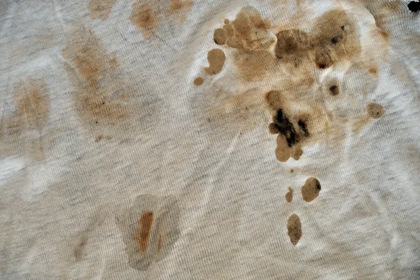 Texture of old dirty torn t-shirt with black-brown spots. Off-white fabric with many spots. Grunge damaged fabric. Crumpled torn rag.
